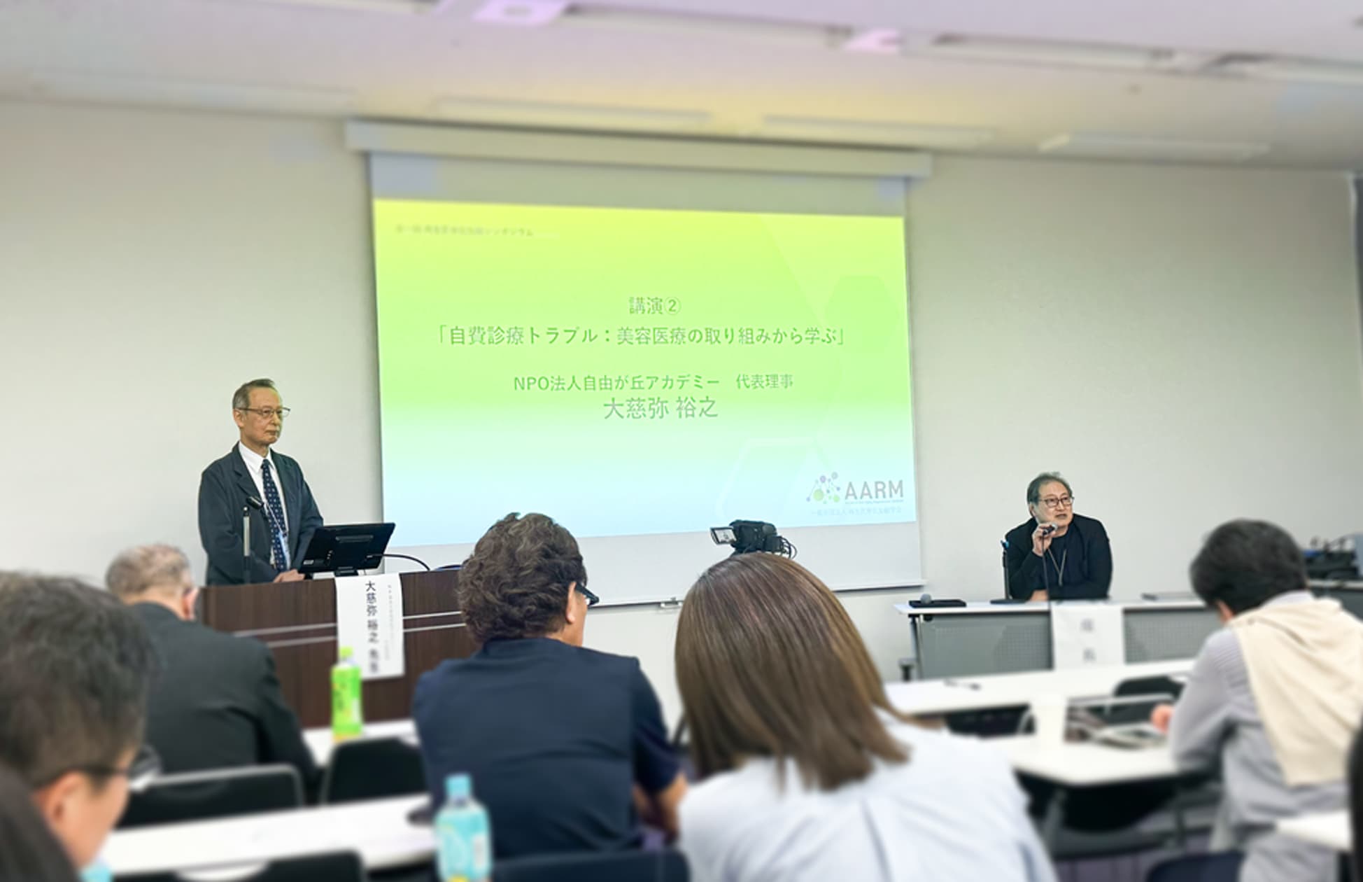 登壇する大慈弥医師と座長の山田医師の写真